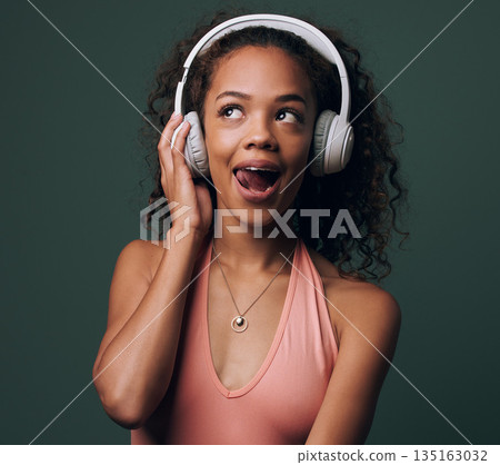 Music, headphones and gen z girl in studio for streaming, silly face or audio on green background. Podcast and goofy female model relax while listening to radio, audio or online playlist 135163032