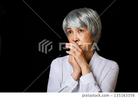A senior woman thinking about something with her hands together and looking into the distance A senior woman thinking about something with her hands together and looking into the distance 135163356