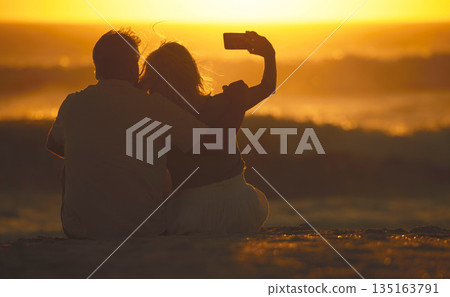 Travel, couple and selfie at sunset on a beach for vacation or holiday outdoor. Behind romantic man and woman in nature with peace, calm and ocean for quality time, love and freedom or photo memory Travel, couple and selfie at sunset on a beach for vacation or holiday outdoor. Behind romantic man and woman in nature with peace, calm and ocean for quality time, love and freedom or photo memory 135163791