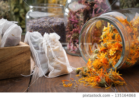 Glass jar of dry calendula flowers and herbal tea bags for alternative medicine and wellness. 135164868