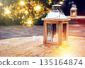 Festive wooden lantern on an outdoor table with Christmas tree lights in the background 135164874