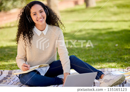 Portrait of happy woman in park studying with headphones, laptop and notes for education in nature, learning and music. Smile, research and university student on grass with audio books for project. Portrait of happy woman in park studying with headphones, laptop and notes for education in nature, learning and music. Smile, research and university student on grass with audio books for project. 135165123