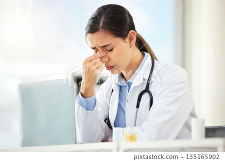 Mental health, woman doctor sad and with laptop at her desk in a modern office with a lens flare. Depression or headache, problem or burnout and female nurse or surgeon fatigue at her workstation 135165902