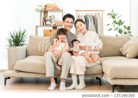 一家人笑容滿面地抱著嬰兒和女兒坐在家裡的沙發上，照片中是父母和孩子。 135166160