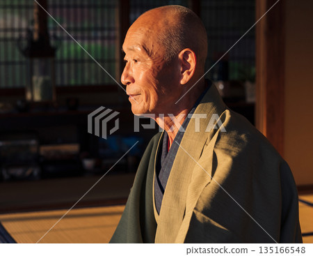 A middle-aged man with a shaved head smiling gently in a Japanese-style room 135166548