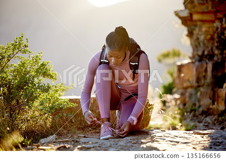 Hiking, shoelace and woman on mountain outdoor with a backpack for adventure and fitness workout. Black athlete person tying shoes for training, exercise or trekking in nature for wellness and travel Hiking, shoelace and woman on mountain outdoor with a backpack for adventure and fitness workout. Black athlete person tying shoes for training, exercise or trekking in nature for wellness and travel 135166656