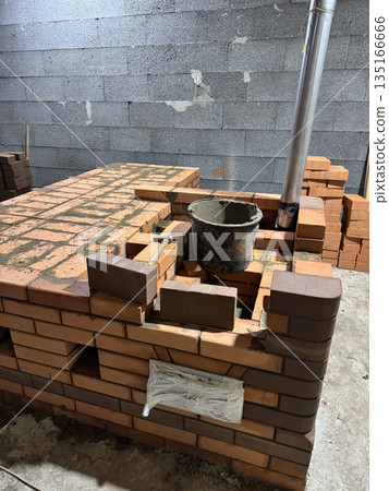 Fresh brickwork of a heating stove with a bench. Metal pipe for convection heating. Fresh brickwork of a heating stove with a bench. Metal pipe for convection heating. 135166666