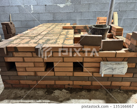 Fresh brickwork of a heating stove with a bench. Cleaning access channels and a metal pipe for convection heating are visible. Fresh brickwork of a heating stove with a bench. Cleaning access channels and a metal pipe for convection heating are visible. 135166667