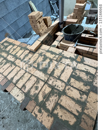 Fresh brickwork of a heating stove with a bench. Metal pipe for convection heating. Oblique Angle. Fresh brickwork of a heating stove with a bench. Metal pipe for convection heating. Oblique Angle. 135166668