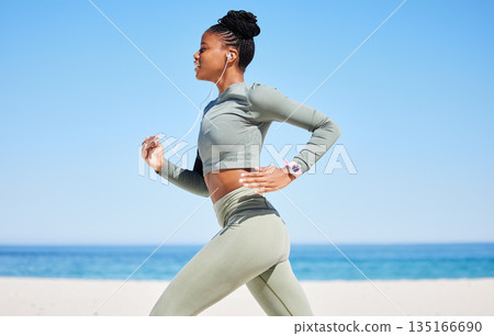 Running, beach and woman listening to music, fitness podcast and training, cardio wellness and health. Ocean, blue sky and african person, runner or athlete exercise, workout and audio technology 135166690