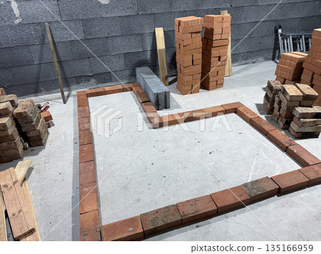 Contour of a heating stove with a bench. Laid out of brick on a concrete screed. Bricks and tools nearby. Contour of a heating stove with a bench. Laid out of brick on a concrete screed. Bricks and tools nearby. 135166959