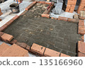 Fresh brickwork of a heating stove with a bench base. Laid out of brick on a concrete screed. Bricks and tools nearby. 135166960