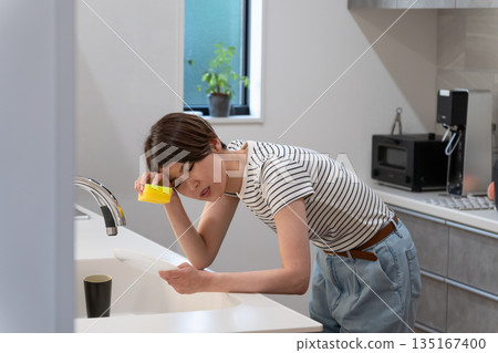 Unwell woman washing dishes in the kitchen Unwell woman washing dishes in the kitchen 135167400