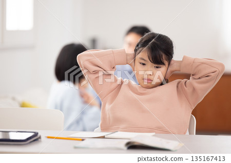 一個小學生女孩雙手抱頭,面前攤開一本課本。 一個小學生女孩雙手抱頭,面前攤開一本課本。 135167413