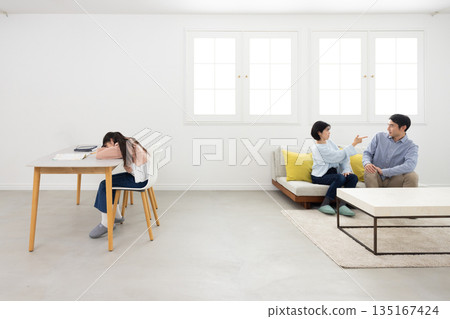 An elementary school girl with her face down on the table near her arguing parents 135167424
