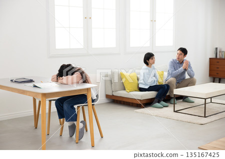 An elementary school girl with her face down on the table near her arguing parents 135167425