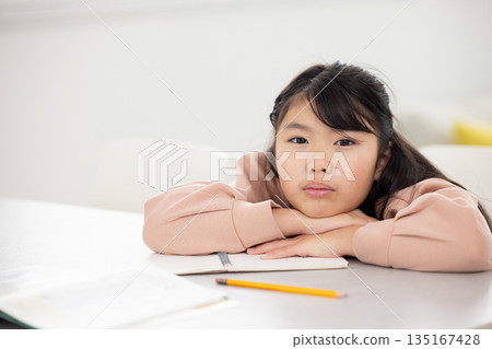 An elementary school girl with a sad expression lying on the table 135167428
