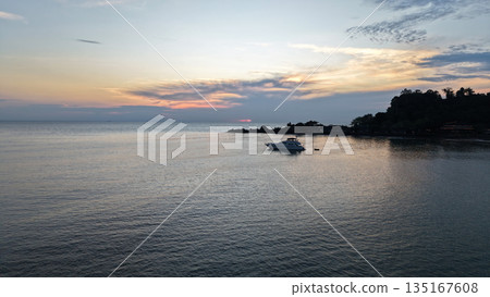 Luxury yacht moored near tropical island at sunset reflecting on calm ocean 135167608
