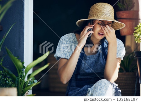 Mental health, woman florist with headache and with smartphone on a phone call with a client at her workplace. Anxiety or stress, sad and female person talking on a cellphone for customer service. Mental health, woman florist with headache and with smartphone on a phone call with a client at her workplace. Anxiety or stress, sad and female person talking on a cellphone for customer service. 135168197
