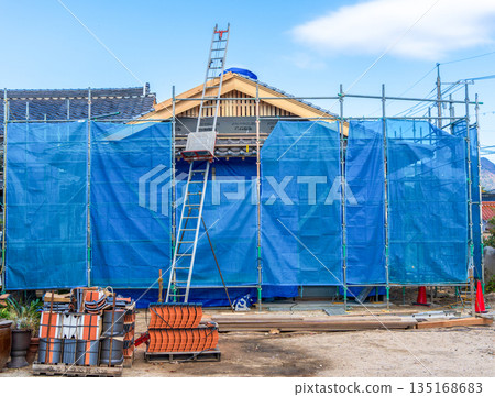 圖:一台瓦片提昇機正在將屋頂瓦片提升到一棟新建的木屋上。 圖:一台瓦片提昇機正在將屋頂瓦片提升到一棟新建的木屋上。 135168683