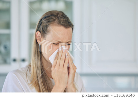 Sick, tissue and woman blowing her nose in the kitchen for a cold, flu or sneeze at her home. Illness, virus and young female person sneezing with allergies, hay fever or covid in her apartment. Sick, tissue and woman blowing her nose in the kitchen for a cold, flu or sneeze at her home. Illness, virus and young female person sneezing with allergies, hay fever or covid in her apartment. 135169140