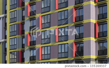 Colorful apartment building facade with bold yellow horizontal stripes and red window accents, Colorful apartment building facade with bold yellow horizontal stripes and red window accents, 135169337
