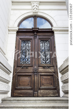 Door with ornate wooden entrance. Old arched front door in historic stone wall, antique architecture Door with ornate wooden entrance. Old arched front door in historic stone wall, antique architecture 135169367