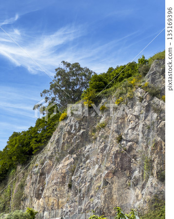 Rock cliff in mountain landscape. Scenic summer view with blue sky, green hill terrain and layered 135169396