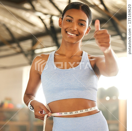 Measure, lose weight or happy woman with thumb up or tape for waist or body goals in fitness studio. Gym, thumbs up or healthy girl measuring her stomach for goal progress, training or motivation 135169620