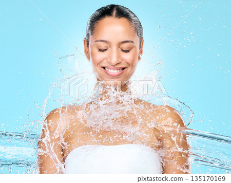 Water, splash and shower with woman in studio for hygiene, beauty and skincare. Wellness, cleaning and fresh with face of female model on blue background for spa, cosmetics and liquid mockup space 135170169