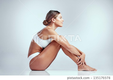 Skincare, woman sitting on the floor and against a white background. Dermatology or cosmetics, body treatment or self care and young female person sit on ground for health wellness against backdrop Skincare, woman sitting on the floor and against a white background. Dermatology or cosmetics, body treatment or self care and young female person sit on ground for health wellness against backdrop 135170378