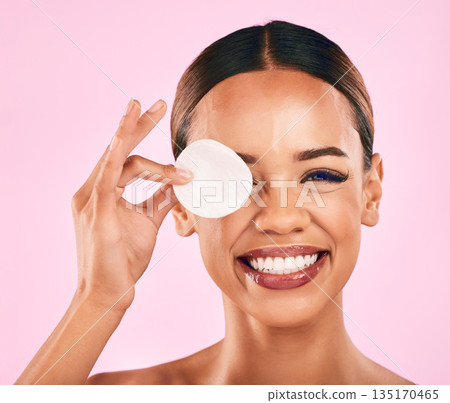 Happy woman, face and cotton pad in makeup removal, skincare or cosmetics against a pink studio background. Portrait of excited female person with cosmetic swab in beauty cleaning or facial treatment 135170465