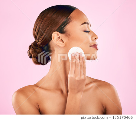 Woman, face and cotton pad in skincare for makeup removal or cosmetics against a pink studio background. Female person or model in relax with cosmetic swab for beauty, cleaning or facial treatment Woman, face and cotton pad in skincare for makeup removal or cosmetics against a pink studio background. Female person or model in relax with cosmetic swab for beauty, cleaning or facial treatment 135170466