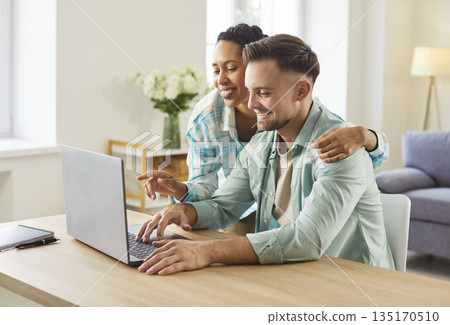 Smiling couple using laptop together at home table, planning finances online Smiling couple using laptop together at home table, planning finances online 135170510