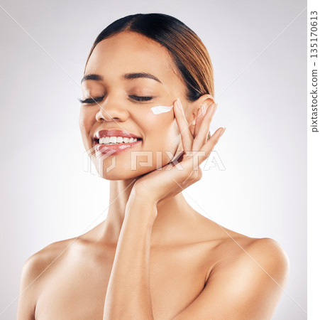 Woman, cream on face and beauty with skincare, smile and moisturizer isolated on studio background. Happy female model apply lotion, dermatology and cosmetic product with skin glow and facial 135170613