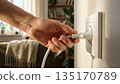 Close up of hand inserting electrical plug into wall socket. 135170789
