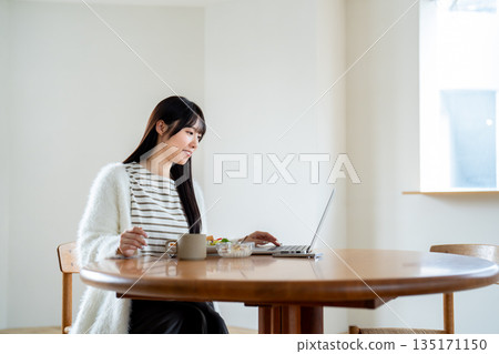 一位女士在餐桌旁使用筆記型電腦工作。 135171150