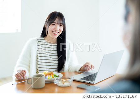 一名女子一邊使用電腦，一邊與對面的人交談（過肩鏡頭） 135171167