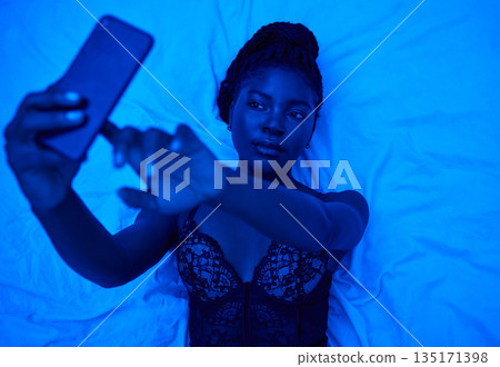 Sexy selfie, bed and black woman with lighting for a photo for social media or online chat. Above, blue room and an African person taking pictures on a mobile in lingerie for web, an app or sexting Sexy selfie, bed and black woman with lighting for a photo for social media or online chat. Above, blue room and an African person taking pictures on a mobile in lingerie for web, an app or sexting 135171398