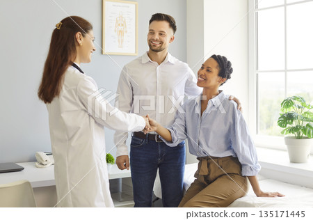 Female doctor greeting smiling couple at medical clinic during checkup today Female doctor greeting smiling couple at medical clinic during checkup today 135171445
