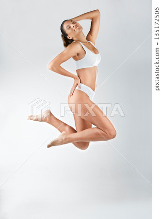 Jump, portrait and a happy woman and active in underwear isolated on a white background in a studio. Smile, carefree and a young lady in a bikini, jumping with happiness or wellness on a backdrop 135172506