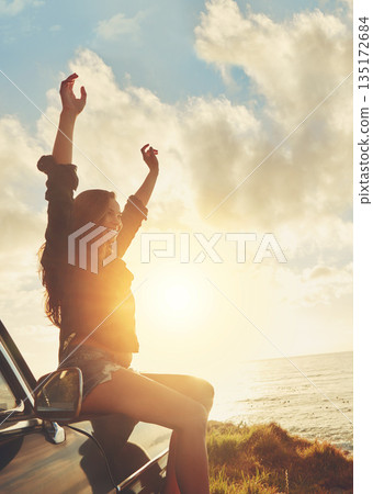 Road trip, view and arms raised with a woman at the coast, sitting on her car bonnet during travel for freedom or escape. Nature, flare and water with a female tourist traveling in summer at sunset Road trip, view and arms raised with a woman at the coast, sitting on her car bonnet during travel for freedom or escape. Nature, flare and water with a female tourist traveling in summer at sunset 135172684