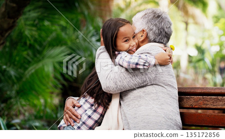 Happy, young girl and grandmother hug or a flower for senior woman or child with care or bond with pensioner and summer day in the park. Joy, kid and elderly person embrace on the bench with love 135172856
