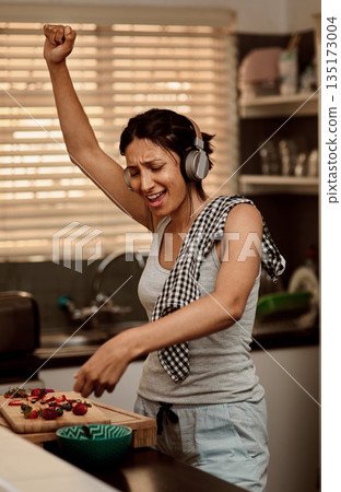 Music headphones, singing and woman cooking with strawberry. Sing, kitchen and female person making snack with fruit for healthy nutrition while dancing to audio, sound and radio podcast in home. Music headphones, singing and woman cooking with strawberry. Sing, kitchen and female person making snack with fruit for healthy nutrition while dancing to audio, sound and radio podcast in home. 135173004