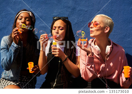 Bubbles women and diverse friends on summer vacation, holiday travel or bonding activity and against a blue wall. Happy, game and ladies playing with soap or wand toy or in freedom and social break 135173010
