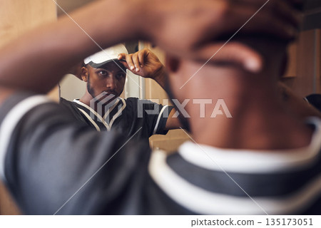 Baseball player, cap and face of sports man in a locker room getting ready and dressing in mirror. Behind an African athlete person with reflection and hat for sport competition, training or exercise 135173051