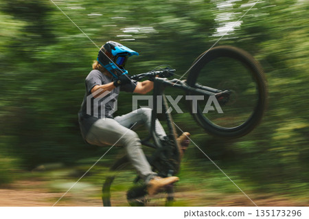 Fitness, trail and man doing a trick on a bike while riding for competition practice in the woods. Extreme sports, blur motion and male athlete biker with skill training or exercise in outdoor forest 135173296