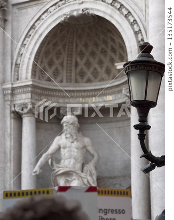 Stone statue in a niche beneath an ornate arch with carved latticework, part of a classical Roman building facade. 135173544