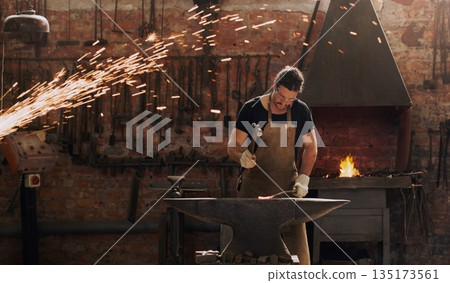 Hammer, anvil and fire with a man working in a factory for metal work manufacturing or production. Industry, welding and trade with a male blacksmith at work in a forge, plant or industrial workshop Hammer, anvil and fire with a man working in a factory for metal work manufacturing or production. Industry, welding and trade with a male blacksmith at work in a forge, plant or industrial workshop 135173561