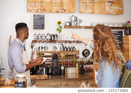 Woman, cafe and pointing at menu on wall with barista, notes and decision for good customer experience. Male waiter writing, lady and talking with choice, thinking and order special from bakery shop 135173960